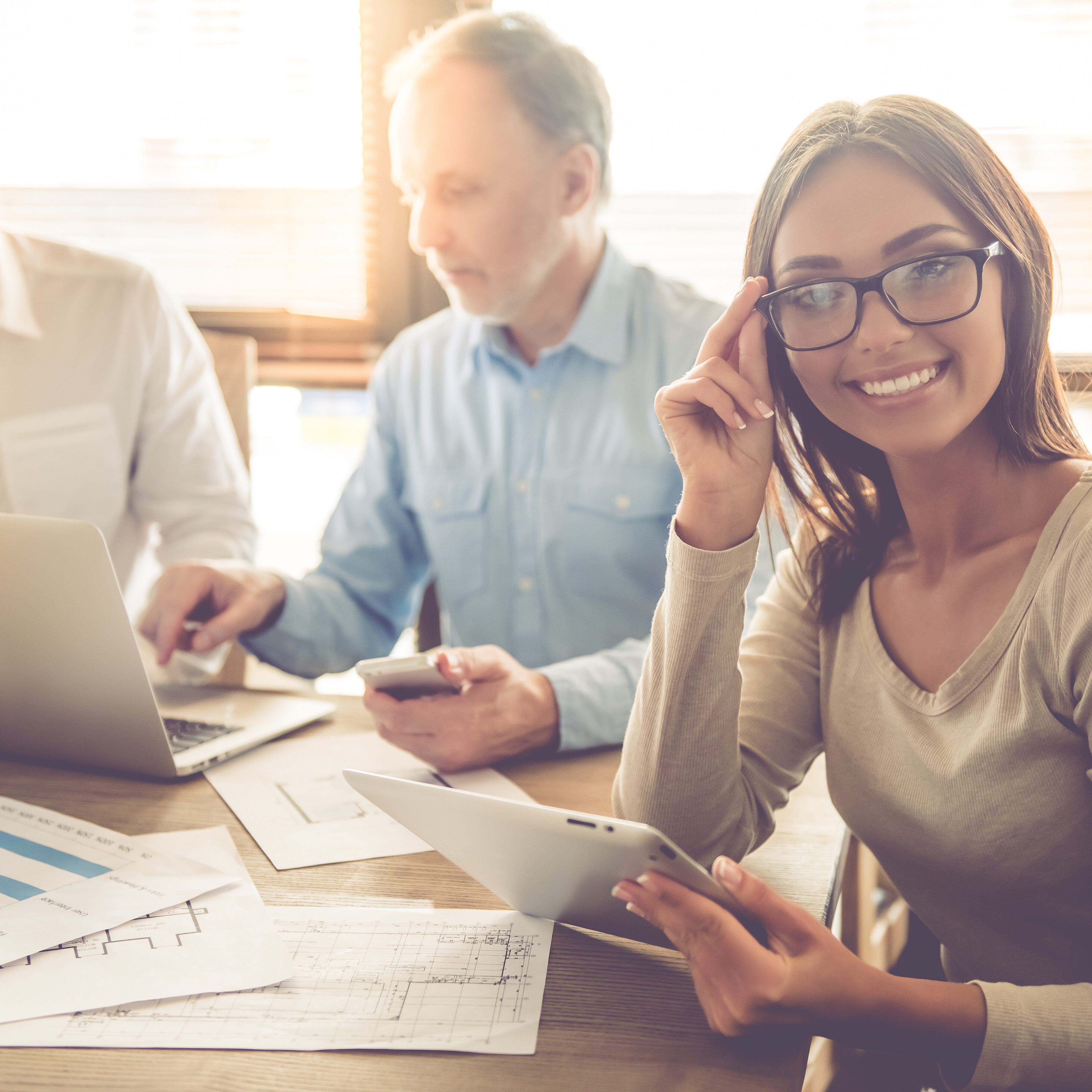 Beautiful business people are using gadgets and discussing affairs while working in office. Business lady is looking at camera and smiling